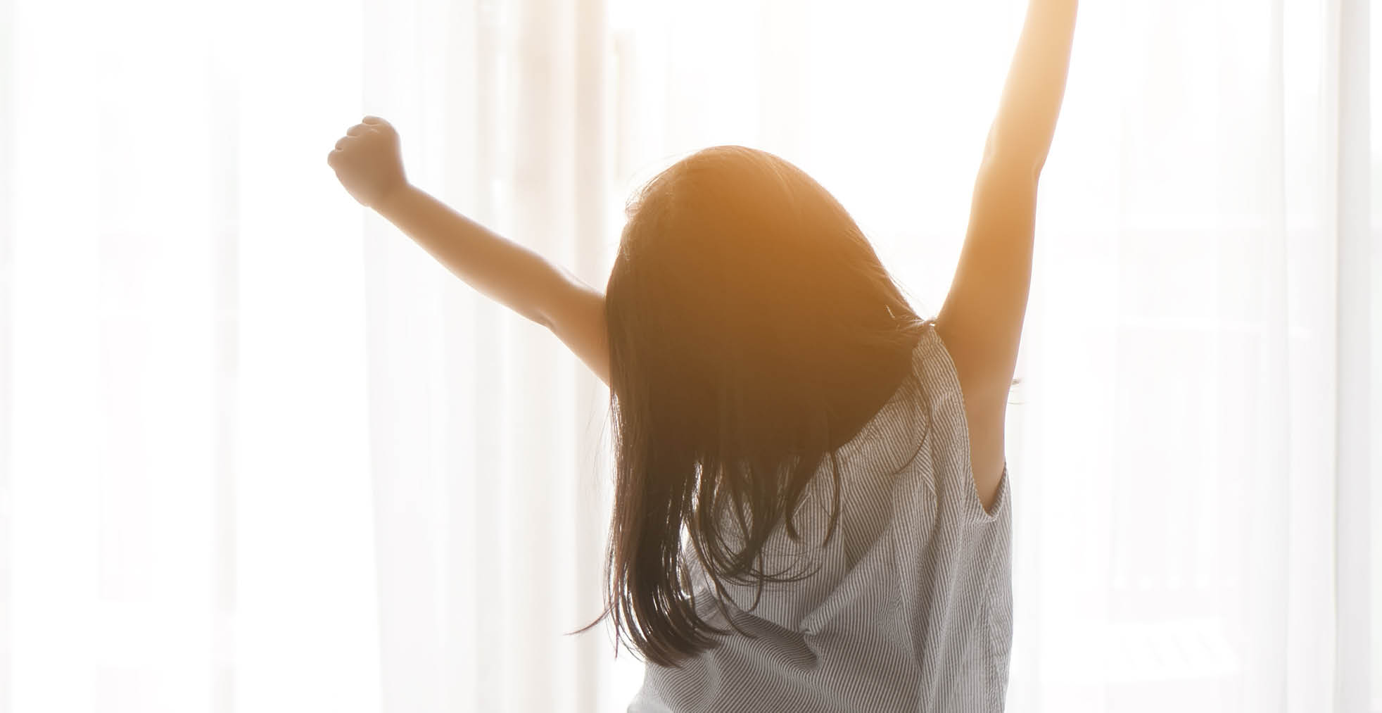 Asian child cute relax or kid girl wake up or woke up with stretch oneself after refreshing sleep in morning on white bed and window with curtain in bedroom at home or hotel on holiday warm sunlight