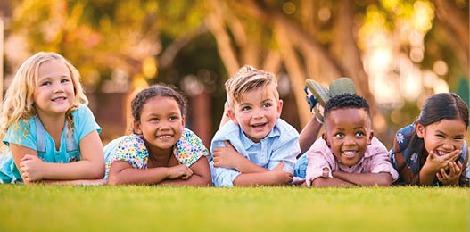 Portrait Of Multi-Cultural Primary Or Elementary School Student Friends Lying On Grass Outdoors