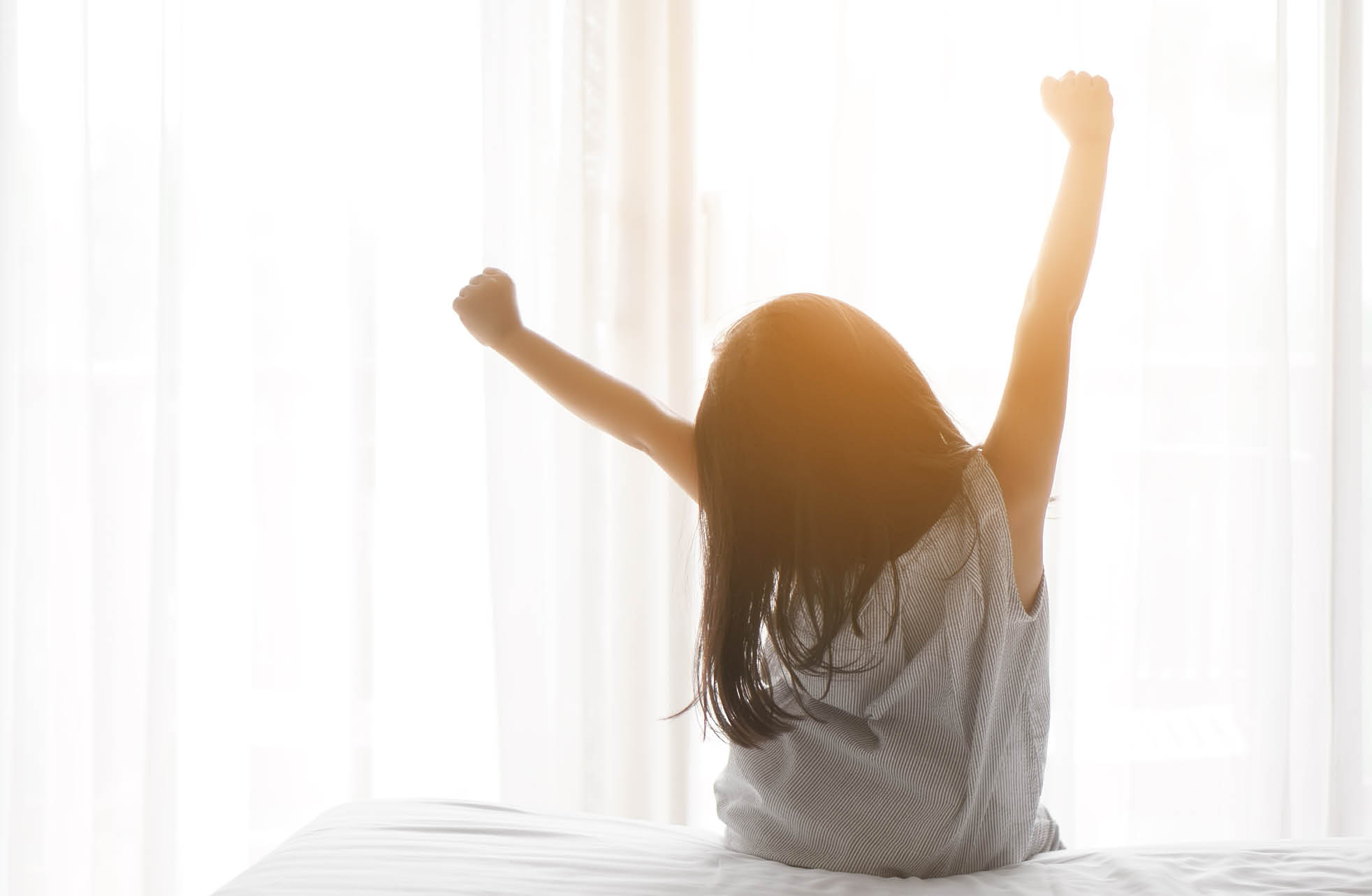 Asian child cute relax or kid girl wake up or woke up with stretch oneself after refreshing sleep in morning on white bed and window with curtain in bedroom at home or hotel on holiday warm sunlight