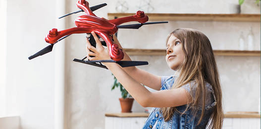 Young cute girl holding quadcopter at home. Child playing with drone. Education, home studying, children, technology, science, future and people concept
